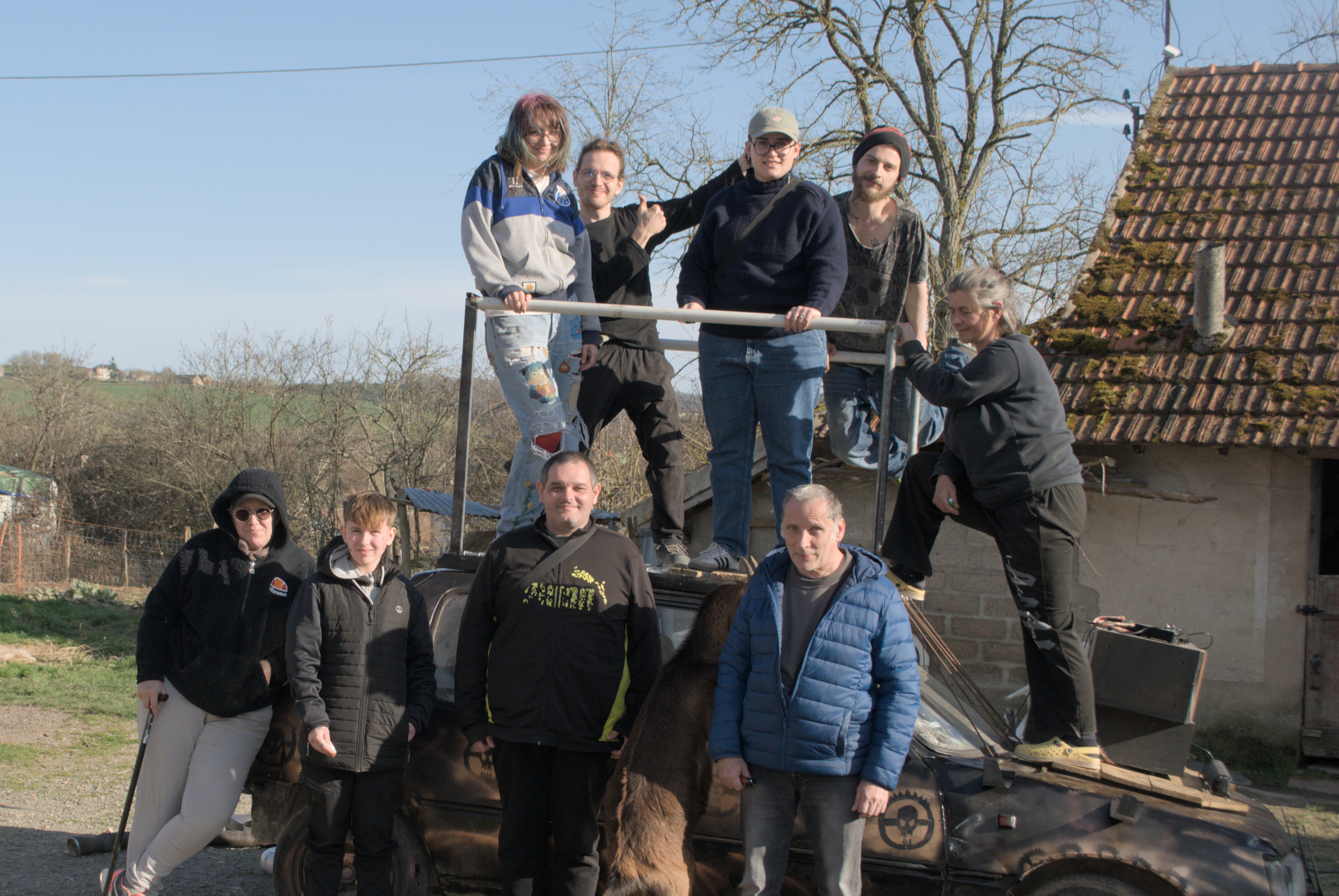 Groupe de stagiaires avec les encadrant·es autour d’une 205 décorée avec de la bombe chromée.
Sur le toit du véhicule, une structure métallique portant quatre personnes est soudée sur l’habitacle.